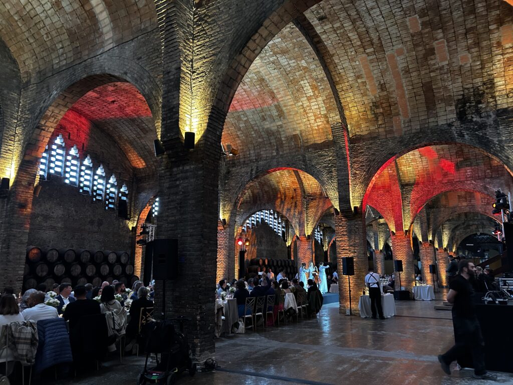 Guests seated at dinner beneath illuminated brick arches at Codorníu, with musicians performing in the background.